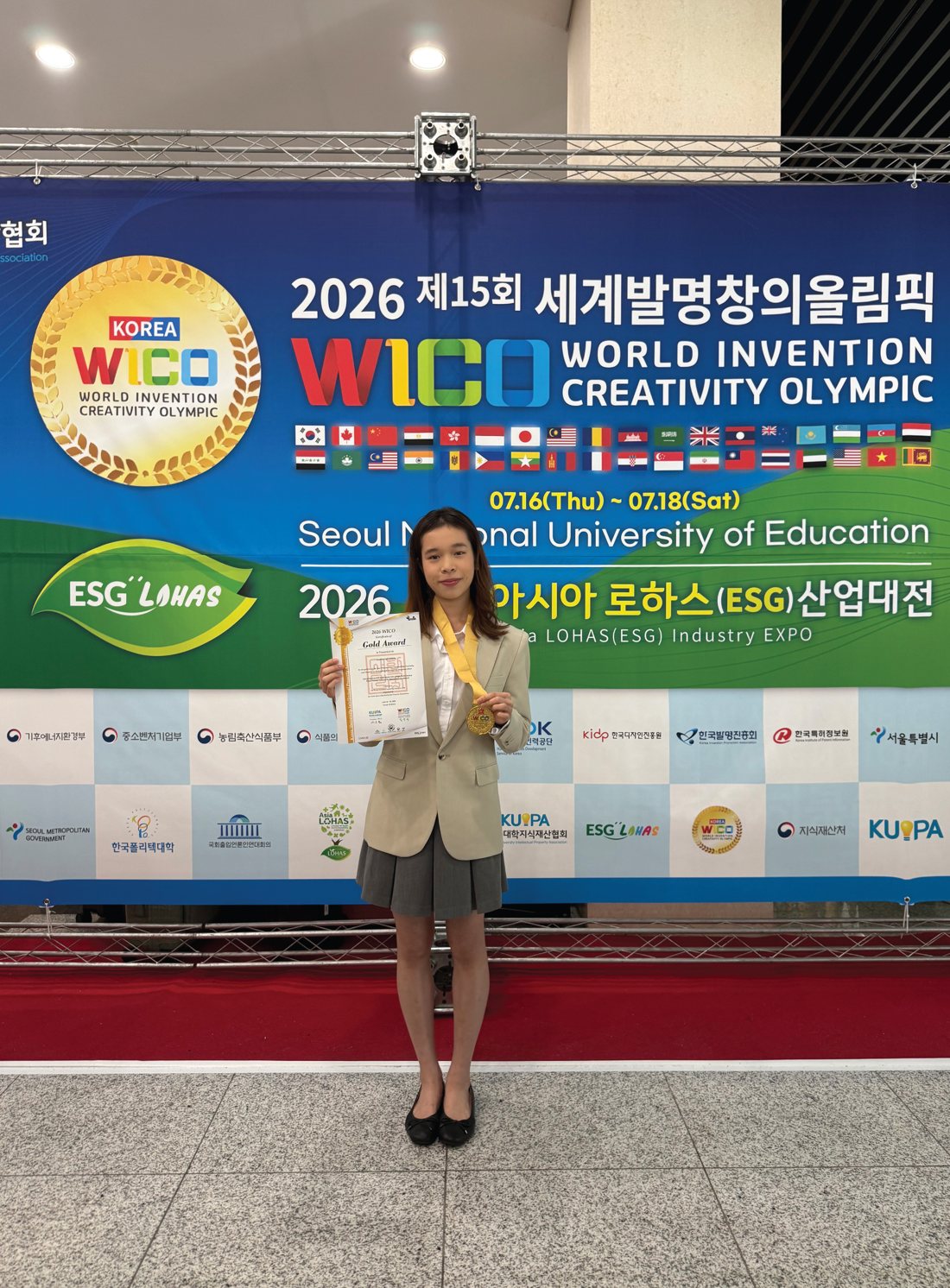 Annie holding her WICO 2026 Gold Award certificate and medal in front of the event banner
